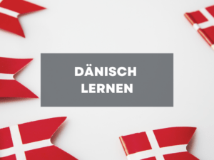 Kleine dänische Flaggen liegen verteilt auf einer weißen Unterlage mit dem Text "Dänisch lernen"